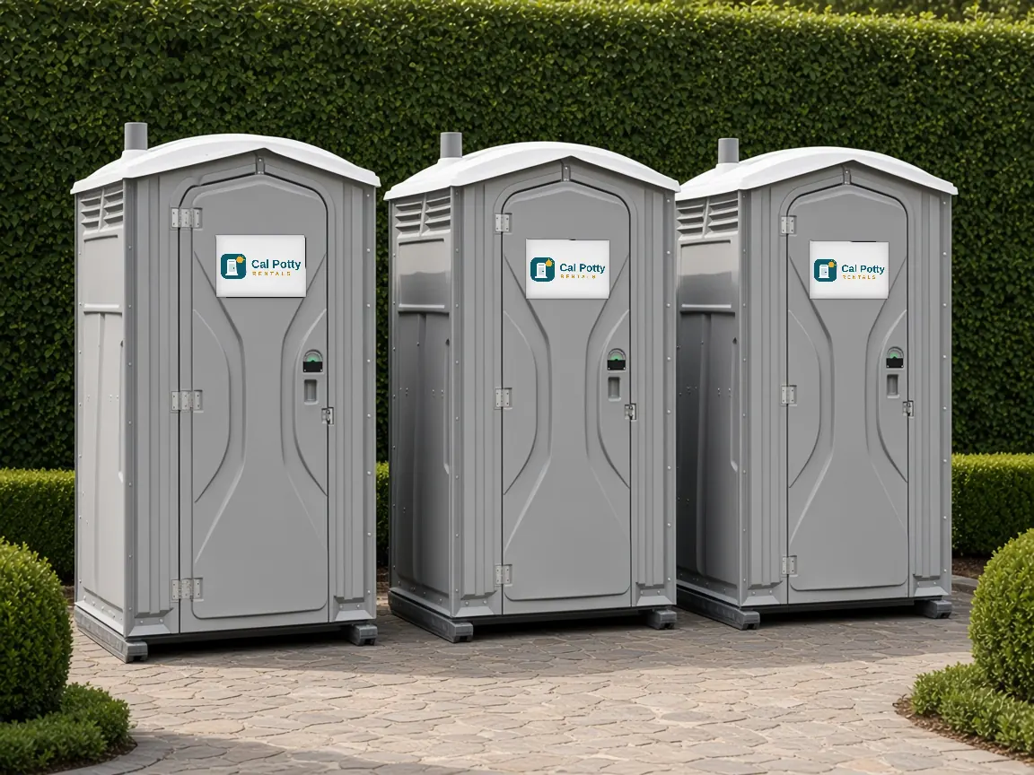 Three grey porta potties in front of a hedge on a paver patio, an example setup for porta potty rental in Menlo Park